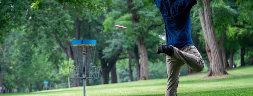 Mann auf Wiese spielt Disc Golf